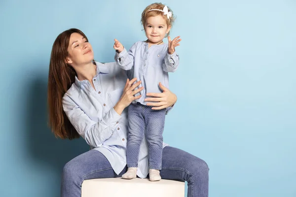 Studio photo de belle femme heureuse et petit enfant, mère et fille isolées sur fond bleu. Fête des Mères. Concept de famille, enfance — Photo