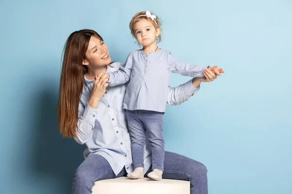 Studio photo de belle femme heureuse et petit enfant, mère et fille isolées sur fond bleu. Fête des Mères. Concept de famille, enfance — Photo