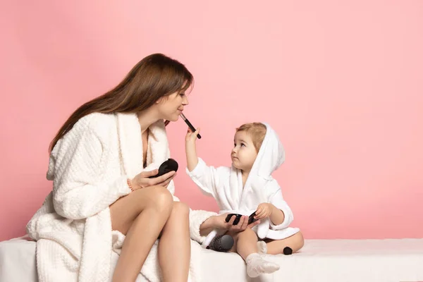 Jeune belle femme heureuse et petit enfant, mère et fille portant un peignoir s'amusant isolé sur fond rose. Fête des mères, famille, enfance — Photo