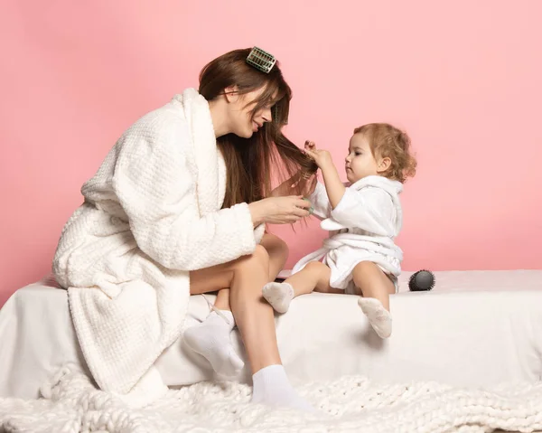 Молода красива щаслива жінка і маленька дитина, мати і дочка, одягнені в халат, розважаються ізольованими на рожевому тлі. День матері, сім "я, дитинство. — стокове фото
