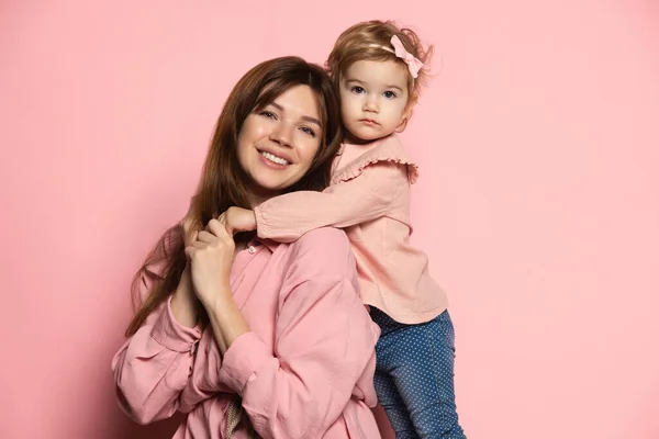 Mujer feliz y niña, madre e hija cariñosas aisladas en el fondo del estudio rosa. Celebración del Día de las Madres. Concepto de familia, infancia, maternidad — Foto de Stock