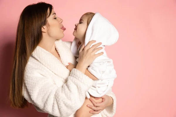 Närbild ung vacker lycklig kvinna och liten unge, mor och dotter bär badrock har kul isolerad på rosa bakgrund. Mors dag, familj, barndom — Stockfoto