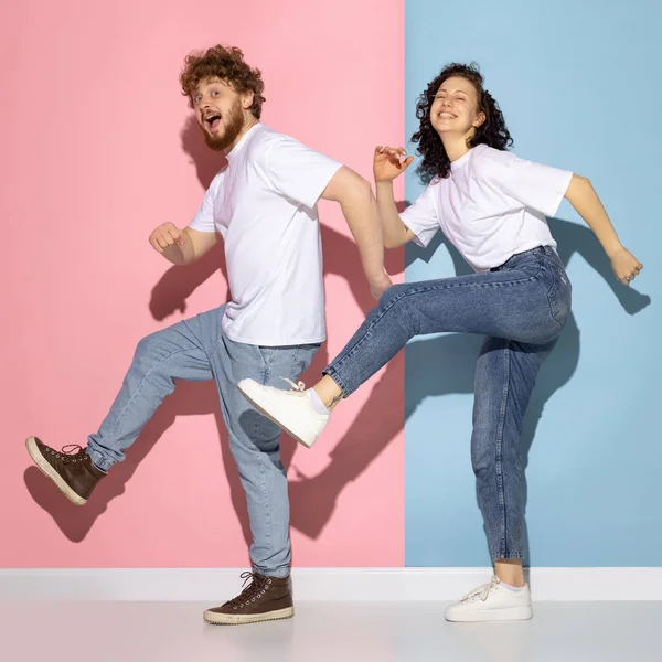 Emotioneel koppel jong grappig en gelukkig man en meisje dansen hip-hop in studio op blauw en roze trendy kleur achtergrond. — Stockfoto