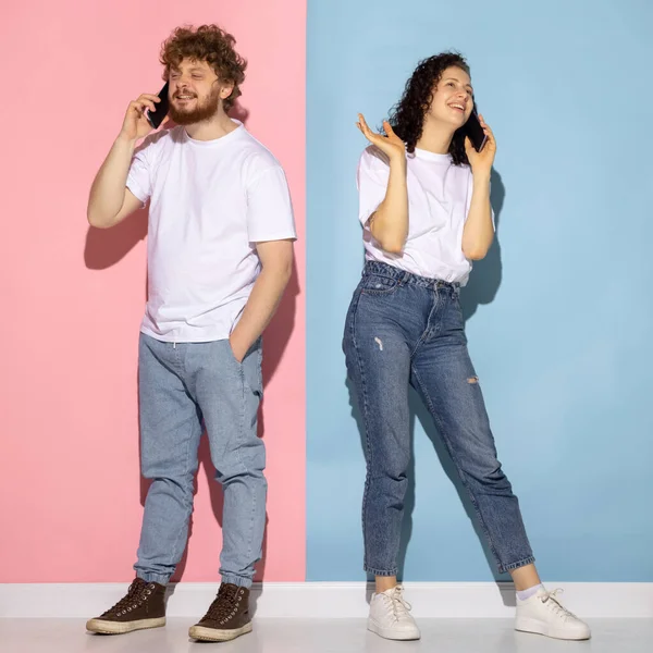 Portrait de jeune homme et fille émotif à l'aide de smartphones isolés sur fond bleu et rose couleur tendance. Concept des émotions humaines — Photo