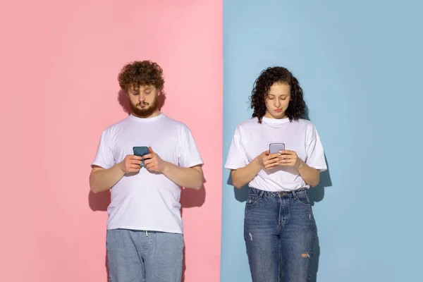 Παντρεμένο ζευγάρι, νεαρός συναισθηματικός άντρας και κορίτσι χρησιμοποιώντας τηλέφωνα απομονωμένα σε μπλε και ροζ μοντέρνο φόντο χρώμα. Ανθρώπινα συναισθήματα, φροντίδα, σχέσεις έννοια — Φωτογραφία Αρχείου