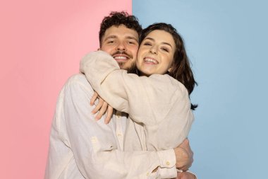 Sarılalım. Mavi ve pembe renkli arka planda izole edilmiş kameraya bakan duygusal erkek ve kızın yarım boy portresi. İnsan duyguları kavramı