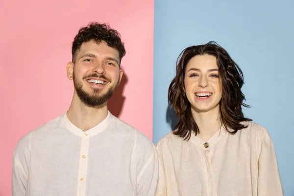 Half length portrait of young emotive man and girl looking at camera isolated on blue and pink trendy color background. Human emotions concept — Stock Photo, Image