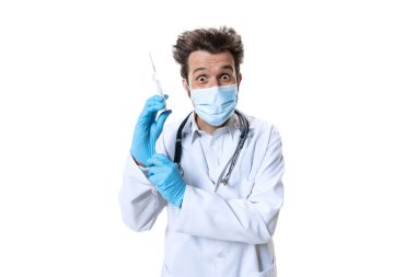 Enjeksiyon için hazır. Beyaz stüdyo geçmişinde steteskop ve yüz maskesi olan genç bir erkek doktor. Üzücü ve ciddi görünüyor. Sağlık ve ilaç kavramı, savaş, yardım, tedavi