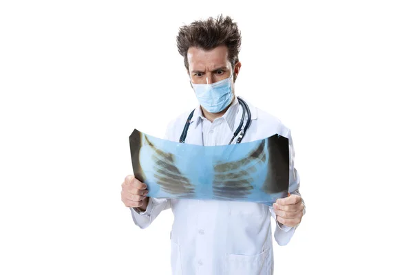 Νεαρός γιατρός με στηθοσκόπιο και μάσκα προσώπου σε λευκό φόντο στούντιο. Φαίνεται λυπημένος, σοβαρός. Έννοια της υγειονομικής περίθαλψης και της ιατρικής, πόλεμος, βοήθεια, θεραπεία — Φωτογραφία Αρχείου