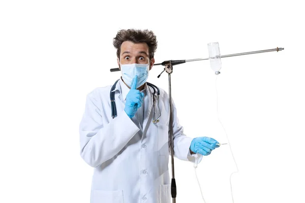 Мужчина молодой врач со стетоскопом и маской на белом фоне студии. Выглядит грустно, серьезно. Концепция здравоохранения и медицины, войны, помощи, лечения — стоковое фото