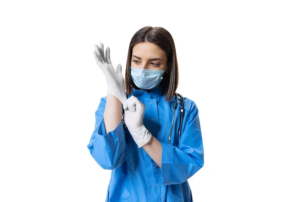 Studio shot of young serious woman, doctor wearing face mask and blue uniform isolated on white background. — Stock Photo, Image