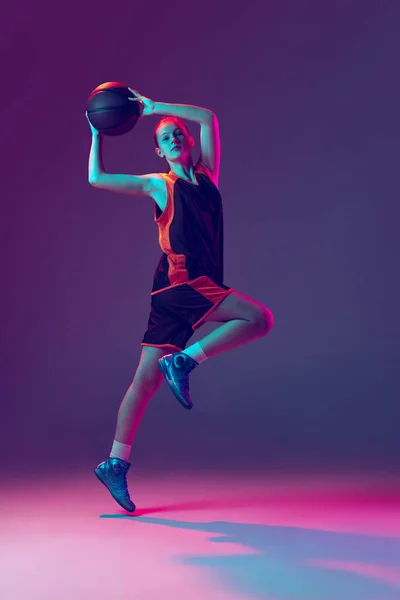 Portret van jong sportief meisje in beweging, basketbal spelen, training geïsoleerd over gradiënt roze paarse achtergrond in neon — Stockfoto