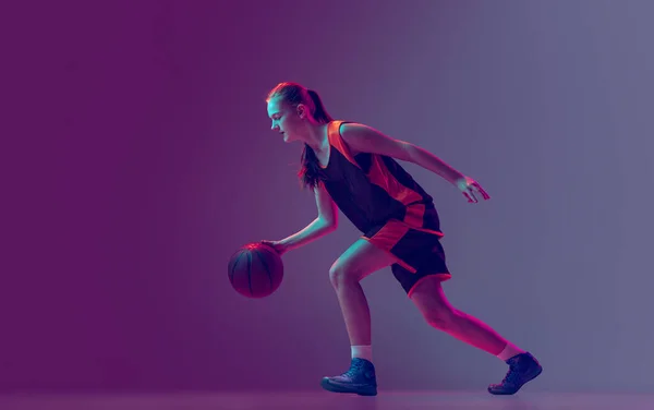Retrato de chica joven, adolescente, jugador de baloncesto en movimiento, entrenamiento aislado sobre fondo rosa púrpura degradado en neón. Vista lateral — Foto de Stock