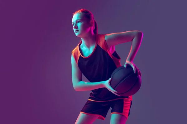 年轻的女运动员的画像，篮球运动员的训练，准备抛出一个孤立在深紫色背景之上的球 — 图库照片