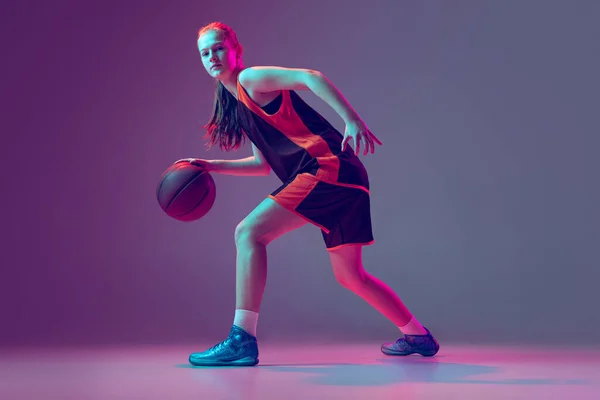 Retrato de chica joven, adolescente, jugador de baloncesto en movimiento, entrenamiento aislado sobre el gradiente rosa púrpura fondo en neón — Foto de Stock