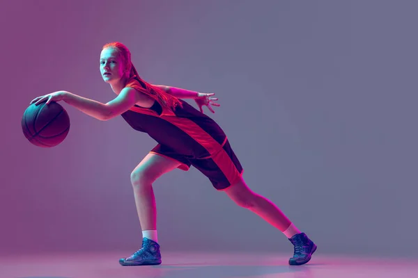 Portret van jong meisje, tiener, basketbalspeler in beweging geïsoleerd over gradiënt roze paarse achtergrond in neon. Professionele speler — Stockfoto