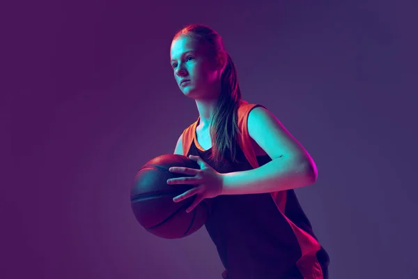Πορτρέτο της νεαρής κοπέλας, μπασκετμπολίστας σε καφέ ομοιόμορφη εκπαίδευση απομονωμένη πάνω από κλίση ροζ μωβ φόντο σε νέον. — Φωτογραφία Αρχείου