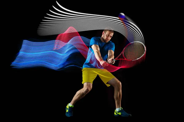 Portrait dynamique d'un homme caucasien jouant au tennis isolé sur fond sombre avec des stipes de couleur mélangée. Concept de sport, passe-temps, défis, paix, politique — Photo