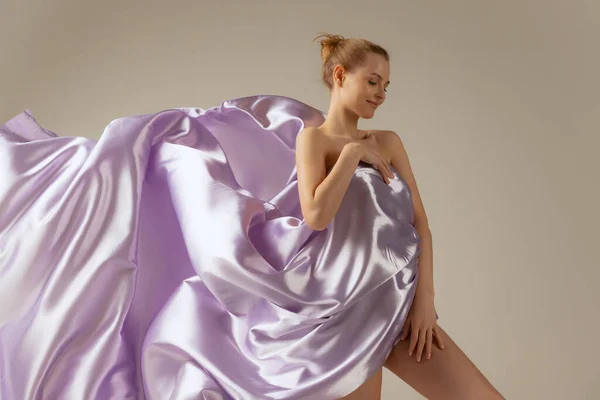 Retrato de media longitud de una hermosa mujer cubierta con tela de seda voladora, posando aislada sobre fondo beige del estudio — Foto de Stock
