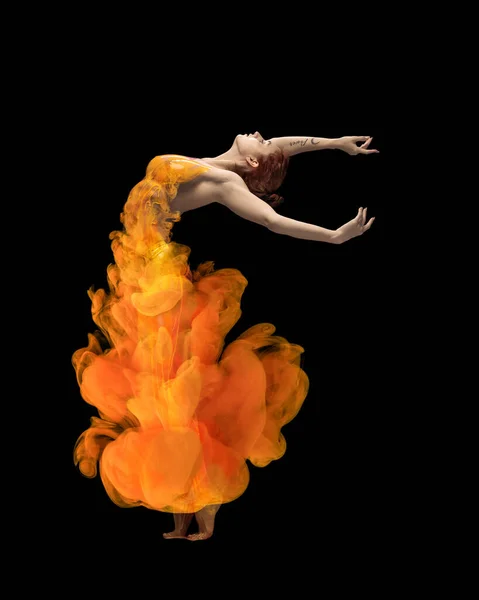 Полнометражный портрет молодой эмоциональной женщины, покрытой оранжевым брызгом, танцующей, позирующей изолированно на черном фоне — стоковое фото