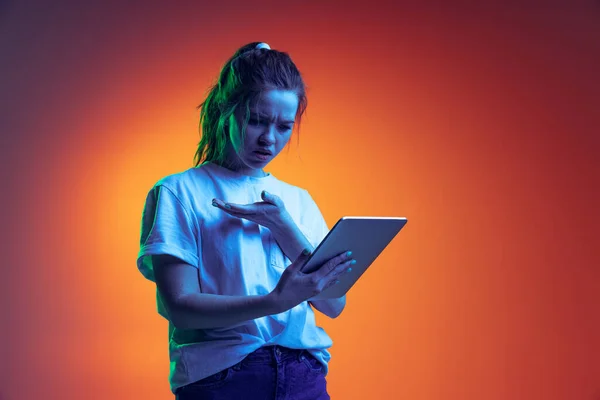 Halve lengte portret van jong meisje met online video oproep op tablet geïsoleerd over gradiënt rode achtergrond in blauw neon licht — Stockfoto