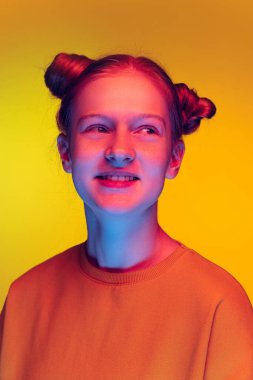 Stüdyo portresi turuncu kazaklı güzel bir kız gülümsüyor, sarı arka planda, neon ışıkta izole bir şekilde poz veriyor.