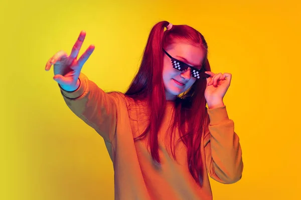 Portret van tiener meisje in pixel zonnebril toont vrede teken met vingers, poseren geïsoleerd over gele studio achtergrond — Stockfoto