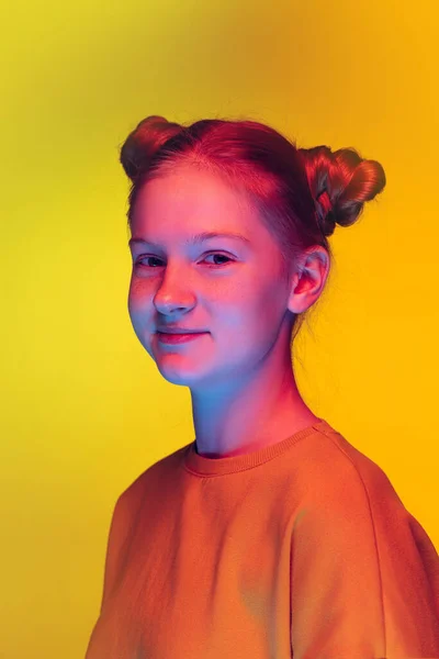 Studio portret van mooi jong meisje in oranje sweater kijken naar camera, poseren geïsoleerd over gele achtergrond in neon licht — Stockfoto