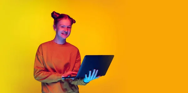 원문 기사보기 컴퓨터를 가진 10 대 소녀가 온라인 동영상 통화를 통해 네온의 옐로우 스튜디오 배경에서 고립된 채웃고 있는 모습 — 스톡 사진