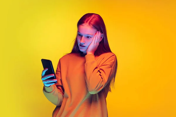 若いです感情的な女の子の肖像上の電話で隔離された上の黄色のスタジオの背景でネオンライト — ストック写真