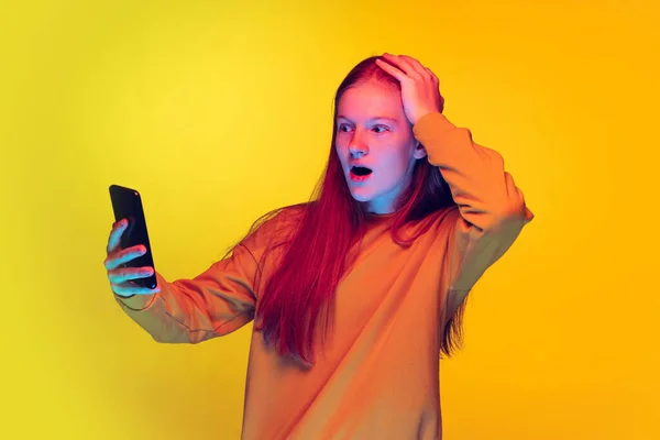 Portré fiatal érzelmes lány miután online video hívás telefonon elszigetelt sárga stúdió háttér neon fény — Stock Fotó