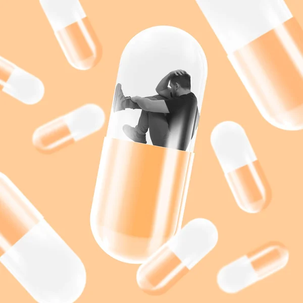 Obra conceptual. Hombre de aspecto desesperado sentado dentro de una píldora gigante que simboliza depresión y problemas de salud mental — Foto de Stock