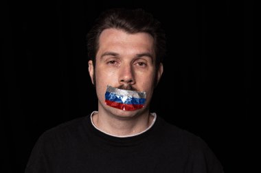 Acıyor. Ağzının üstüne üç renkli koli bandı yapıştırılmış koyu arkaplanda genç bir adamın kavramsal portresi. Sansür, ifade özgürlüğü kavramı.