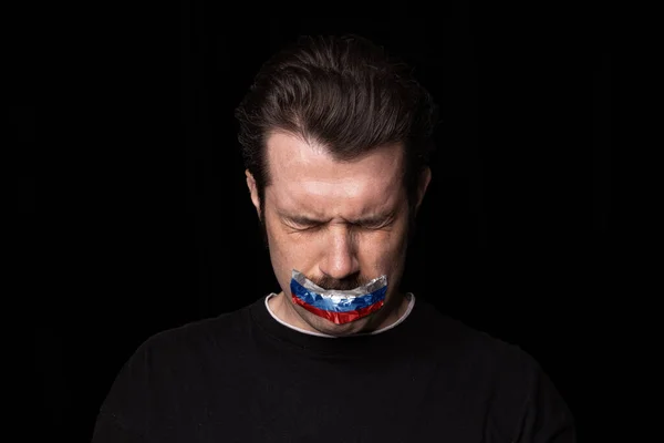 Ritratto concettuale di giovane uomo sconvolto con tre colori nastro adesivo sulla bocca isolato su sfondo scuro. Censura, concetto di libertà di parola. — Foto Stock