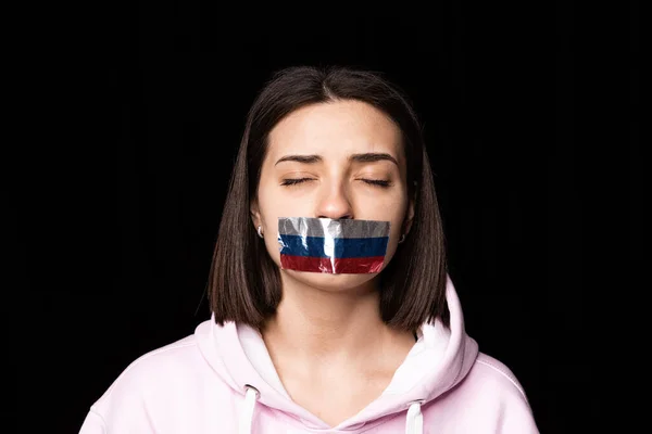 Portrait of young upset girl closed eyes and three colors duct tape over her mouth isolated on dark background. Censorship, freedom of speech concept. — Stock Photo, Image