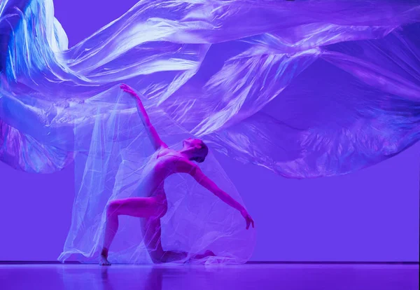 Retrato de bela mulher flexível, bailarina dançando com pano no fundo do estúdio roxo em néon. Moda, estilo, arte, beleza — Fotografia de Stock