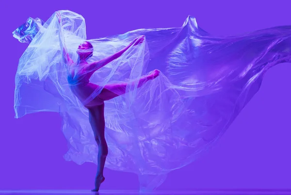 Retrato de bela mulher flexível, bailarina dançando com pano no fundo do estúdio roxo em néon. Moda, estilo, arte, beleza — Fotografia de Stock