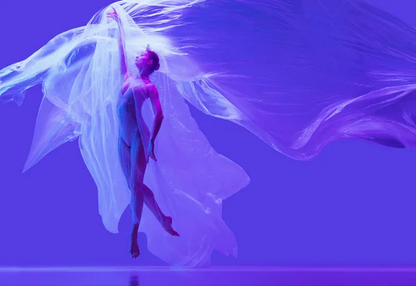 Retrato de bela mulher flexível, bailarina dançando com pano no fundo do estúdio roxo em néon. Moda, estilo, arte, beleza — Fotografia de Stock