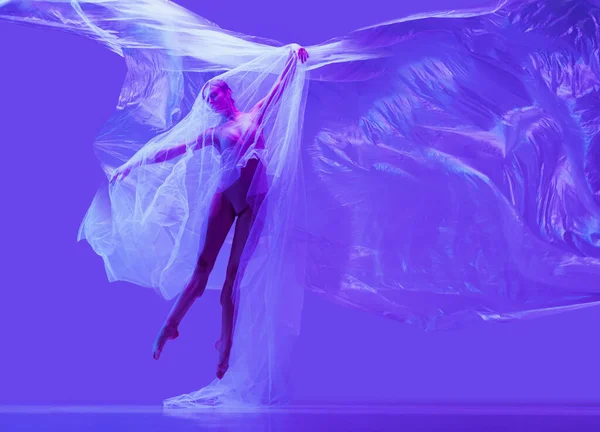 Retrato de bela mulher flexível, bailarina dançando com pano no fundo do estúdio roxo em néon. Moda, estilo, arte, beleza — Fotografia de Stock