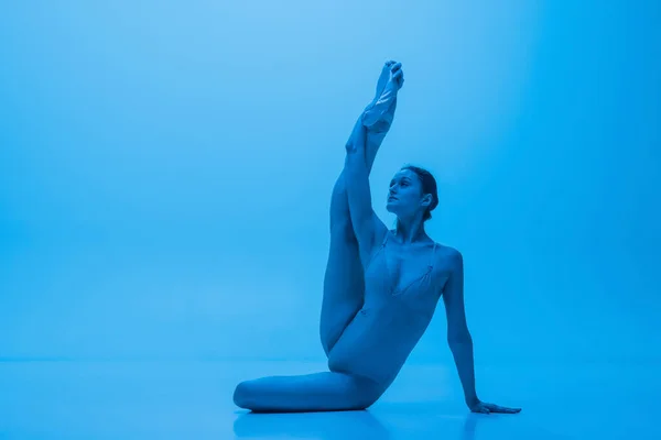 Retrato de bela dançarina de balé graciosa posando isolado no fundo do estúdio azul em luz de néon. Arte, movimento, ação, conceito de flexibilidade. — Fotografia de Stock