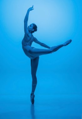 Genç ve zarif balerin mavi stüdyo arka planında neon ışıklarıyla izole edilmiş. Sanat, hareket, eylem, esneklik, ilham kavramı.
