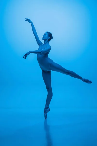 Молодая и изящная балетная танцовщица выделена на фоне синей студии в неоновом свете. Искусство, движение, действие, гибкость, концепция вдохновения. — стоковое фото