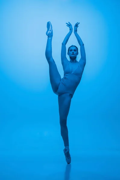 Genade. Jonge en sierlijke balletdanser geïsoleerd op blauwe studioachtergrond in neonlicht. Kunst, flexibiliteit, inspiratie concept. — Stockfoto