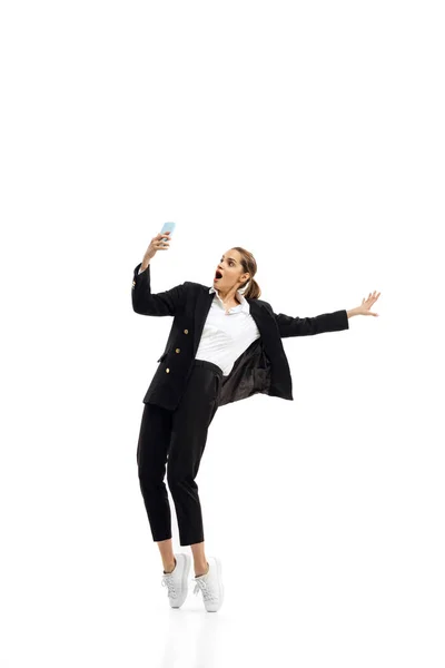 Динамічний портрет молодої жінки, офісного працівника в чорному офіційному костюмі з відеодзвінком по телефону ізольовано на білому фоні студії — стокове фото