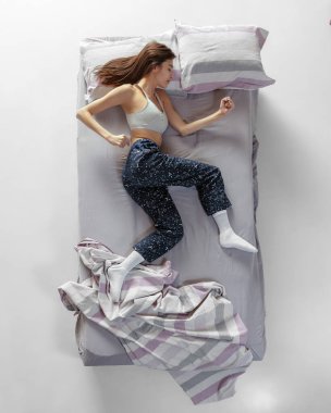 Ev kıyafetleri giymiş, pijamalarıyla büyük gri bir yatakta uyuyan genç bir kızın en iyi manzara portresi. Sağlık kavramı, ev içi, dinlenme zamanı, aile, hayaller