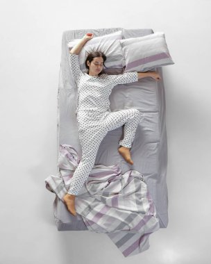 Beyaz pijamalı uyuyan genç bir kız büyük gri bir yatakta yatıyor. Sağlık kavramı, ev içi, dinlenme zamanı, aile, hayaller