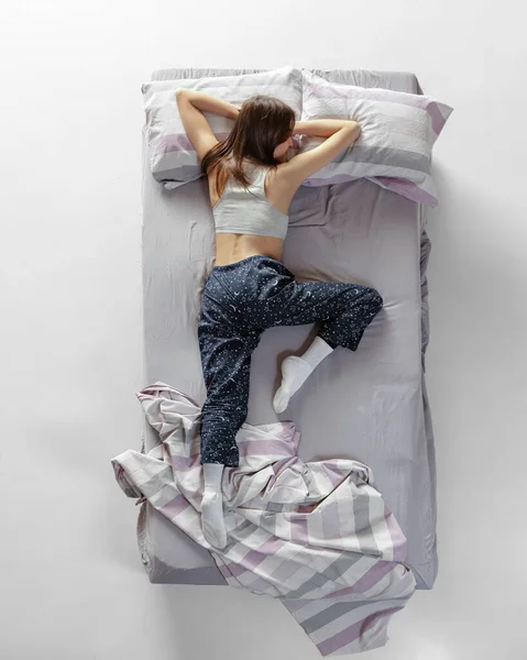 Retrato de vista superior de una joven con ropa de casa, pijamas durmiendo en una gran cama gris. Concepto de salud, interior del hogar, tiempo de relax, familia, sueños —  Fotos de Stock