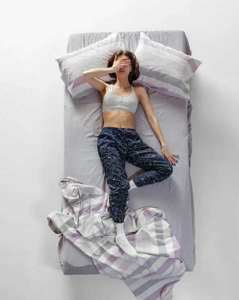 Retrato de vista superior de una joven con ropa de casa, pijamas durmiendo en una gran cama gris. Concepto de salud, interior del hogar, tiempo de relax, familia, sueños —  Fotos de Stock