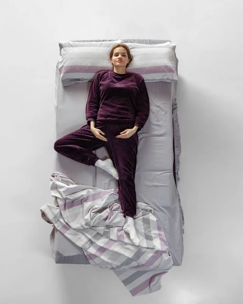Retrato creativo de una joven con ropa de casa de color vino, pijamas durmiendo en una cama grande. Concepto de salud, interior del hogar, tiempo de relax, familia, sueños —  Fotos de Stock
