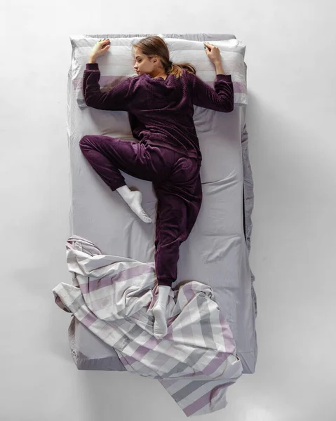 Retrato creativo de una joven con ropa de casa de color vino, pijamas durmiendo en una cama grande. Concepto de salud, interior del hogar, tiempo de relax, familia, sueños — Foto de Stock